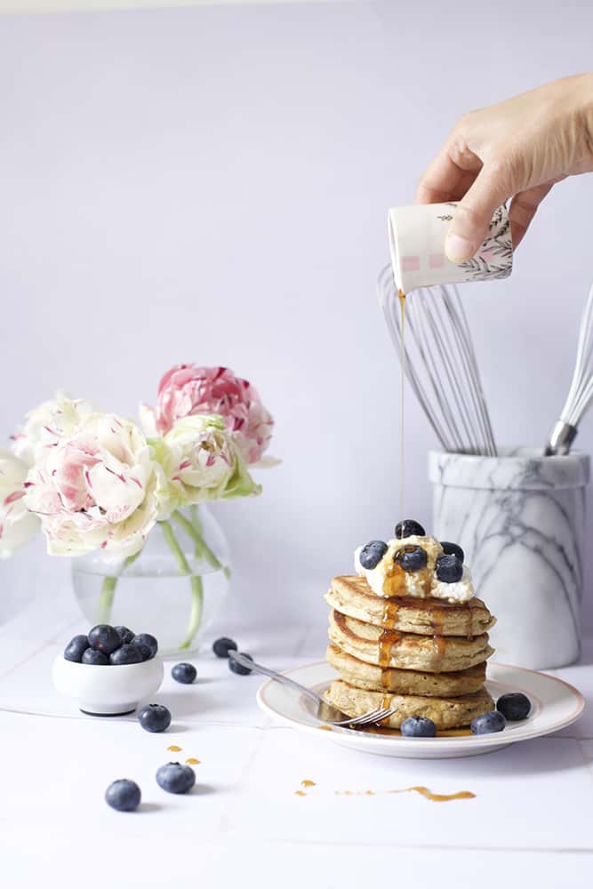 pouring maple syrup on oat flour pancakes